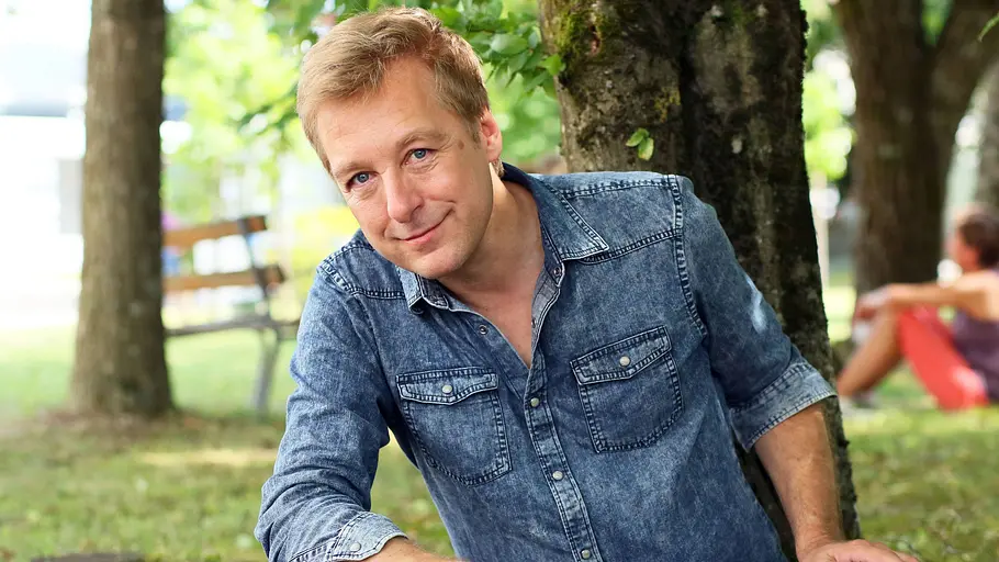 Max Mueller beim - Die Rosenheim Cops - Fantag Max Müller sitzt entspannt unter einem Baum im Grünen und blickt freundlich in die Kamera.