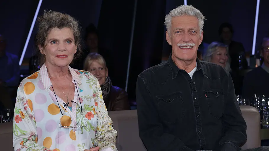 Max und Sonja Moor Sonja Moor in einer bunt gemusterten Bluse und Max Moor in einem schwarzen Hemd sitzen vor Publikum auf einem Sofa.