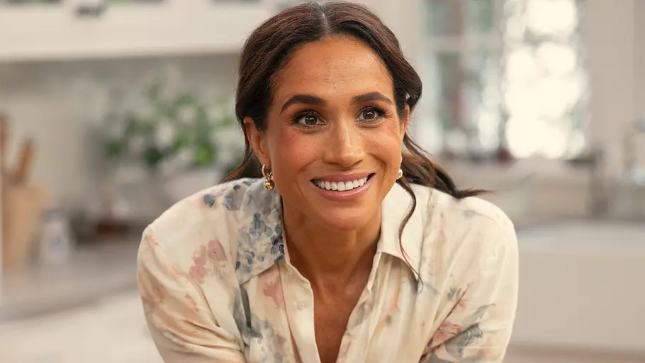 Meghan Markle bei Dreharbeiten zu einem TV-Projekt Meghan Markle lächelt in heller Bluse in einer Küche während eines TV-Drehs.