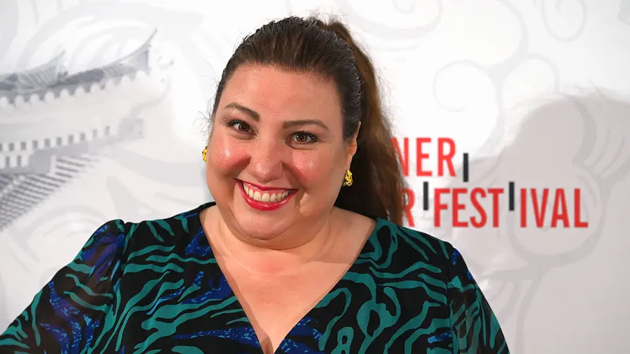 Meltem Kaptan lächelt in die Kamera und steht vor einem hellen Event-Hintergrund mit Schriftzügen.