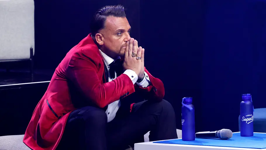 Menowin Fröhlich Menowin Fröhlich sitzt im roten Sakko nachdenklich auf einer Couch im Studio von „Deutschland sucht den Superstar“, die Hände vor dem Gesicht gefaltet.