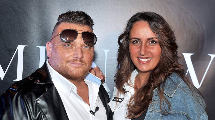Menowin Fröhlich trägt seine Pilotenbrille auf der Stirn und lächelt. Neben ihm steht Senay und legt die Hand auf seine Schulter.