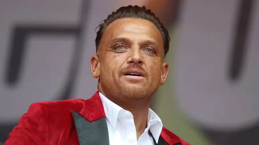 Menowin Fröhlich Menowin Fröhlich gebräunt und in roter Jacke auf der Bühne.