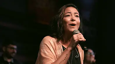 Mica Miller singt in ein Mikrofon. - Foto: © 2026 Netflix, Inc. Mica Miller singt in ein Mikrofon. - Foto: © 2026 Netflix, Inc.
