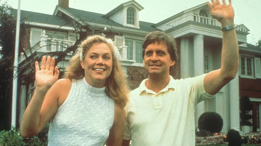 Michael Douglas Kathleen Turner Affäre Michael Douglas und Kathleen Turner als Paar vor einem großen Haus mit weißen Säulen und einem gepflegten Garten.