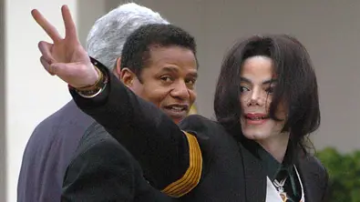 Michale Jackson zeigt mit zwei Fingern „Peace“, während er mit Jackie Jackson in ein Gerichtshaus geht. - Foto:  IMAGO / ZUMA Press