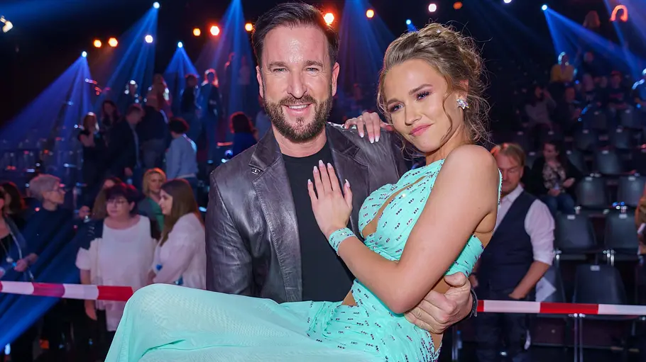 Michael Wendler und Laura Müller Michael Wendler trägt Laura Müller im türkisfarbenen Kleid auf dem Arm. Im Hintergrund sitzen Zuschauer unter blauen Scheinwerfern.