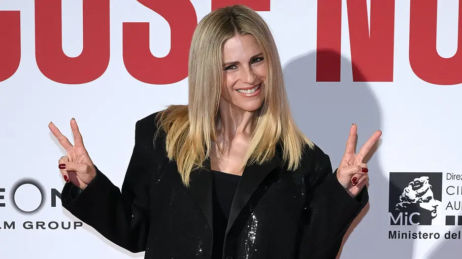 Michelle Hunziker Michelle mit blonden Haaren und schwarzer Jacke posiert auf dem roten Teppich und zeigt mit beiden Händen das Peace-Zeichen.