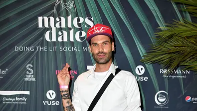 Mike Cees posiert mit roter Cap und weißem Hemd vor einer Fotowand bei einem Event. - Foto: IMAGO / Future Image Mike Cees posiert mit roter Cap und weißem Hemd vor einer Fotowand bei einem Event. - Foto: IMAGO / Future Image