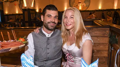 Mike Cees und Michelle Monballijn sitzen lächelnd nebeneinander in einem bayerisch dekorierten Lokal. - Foto: IMAGO / BREUEL-BILD Mike Cees und Michelle Monballijn sitzen lächelnd nebeneinander in einem bayerisch dekorierten Lokal. - Foto: IMAGO / BREUEL-BILD