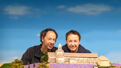 Die Gebrüder Braun lächeln in die Kamera hinter einer Miniatur einer Burg - Foto: B|14 FILM