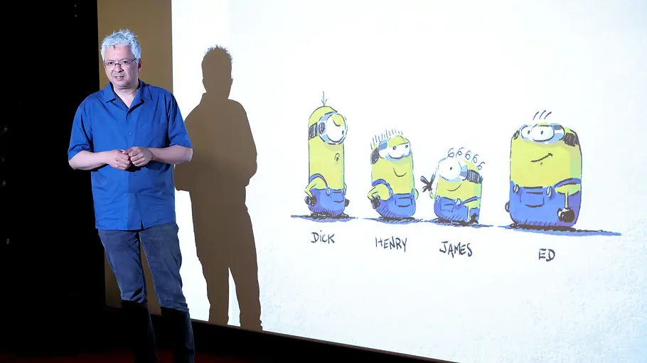 Pierre Coffin steht vor einer Leinwand auf der Zeichnungen von Minions zu sehen sind.