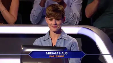 Miriam Haus sitzt mit kurzen braunen Haaren und Jeanshemd hinter einem Bildschirm. Eine Einblendung nennt ihren Namen und Karlsruhe. - Foto: RTL+