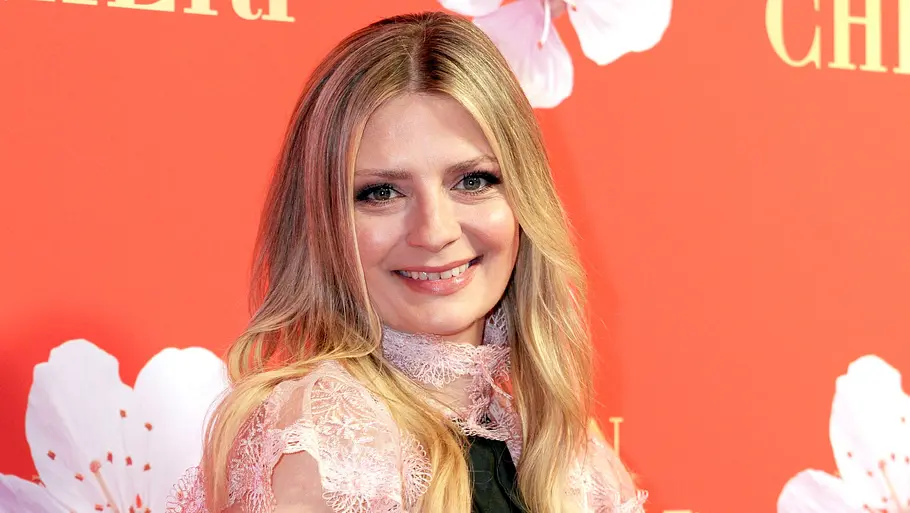 Mischa Barton bei einem Event Mischa Barton lächelt bei einem öffentlichen Auftritt vor einer orangefarbenen Fotowand in die Kamera.