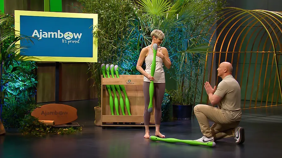 Mit einem Deal hätte der Antrag vielleicht noch ein bisschen mehr Freude gemacht. Susan Schmidt hält ein grünes Trainingsgerät, während Simon Werner neben ihr kniet. Im Hintergrund steht ein Ajambow-Schild.