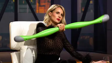 Janna Ensthaler sitzt in schwarzer Spitzenkleidung auf einem weißen Sessel und hält einen langen grünen Stab mit grauen Enden. - Foto: RTL