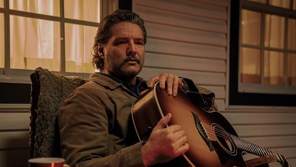 Pedro Pascal als Joel. Er sitzt mit einer Gitarre auf dem Schoß auf der Veranda. - Foto: Liane Hentscher/HBO