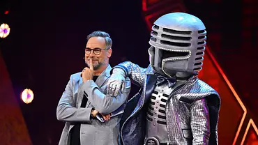 Matthias Opdenhövel steht neben Mr. Mic im silbernen Mikrofonkostüm, der einen Arm auf seine Schulter legt. - Foto: Joyn Matthias Opdenhövel steht neben Mr. Mic im silbernen Mikrofonkostüm, der einen Arm auf seine Schulter legt. - Foto: Joyn