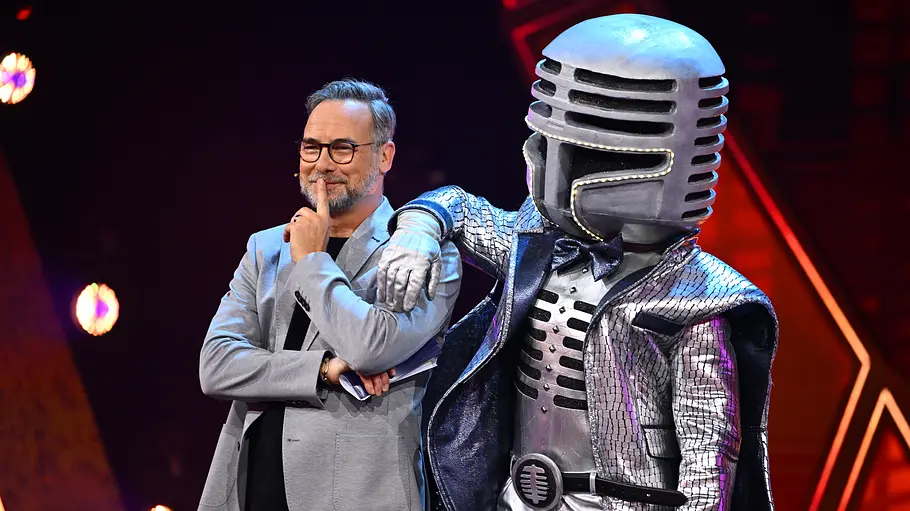 Mit so einem großen Mikrofon kann jeder Matthias Opdenhövel hören. Matthias Opdenhövel steht neben Mr. Mic im silbernen Mikrofonkostüm, der einen Arm auf seine Schulter legt.