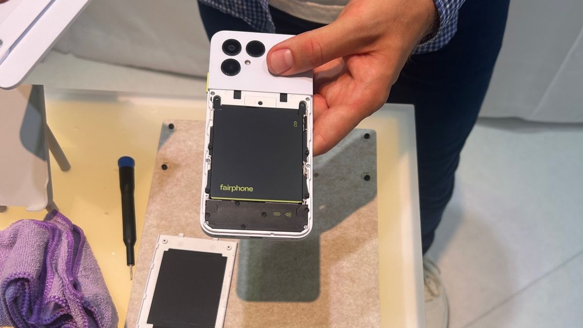 Module Fairphone 6 In der Hand wird ein Smartphone gehalten, auf einem Tisch liegen Ersatzteile und ein Schraubendreher.