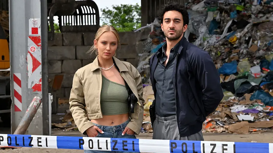 Mord im Revier Handlung & Start Szene aus „Mord im Revier“: Caro Cult als Lou und Eidin Jalali als Gianni stehen hinter Polizeiabsperrband vor einem Müllberg.