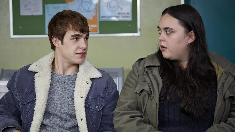 My Mad Fat Diary Zwei Jugendliche sitzen in einem Wartebereich nebeneinander und wechseln einen nachdenklichen Blick. Die Szene stammt aus der britischen Dramaserie „My Mad Fat Diary“.