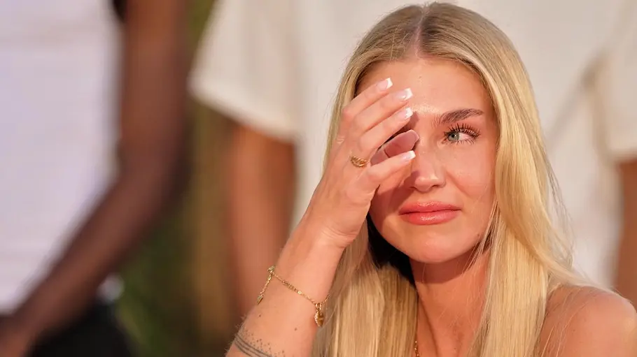 Michelle Michelle wischt sich mit ernstem, emotionalem Gesichtsausdruck eine Träne aus dem Auge und blickt nachdenklich zur Seite.