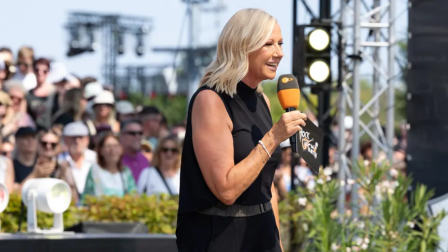 Nach der großen Rockshow am letzten Sonntag darf sich Andrea Kiewel am kommenden Wochenende entspannen. Andrea Kiewel im schwarzen Outfit mit Mikro im Fernsehgarten.