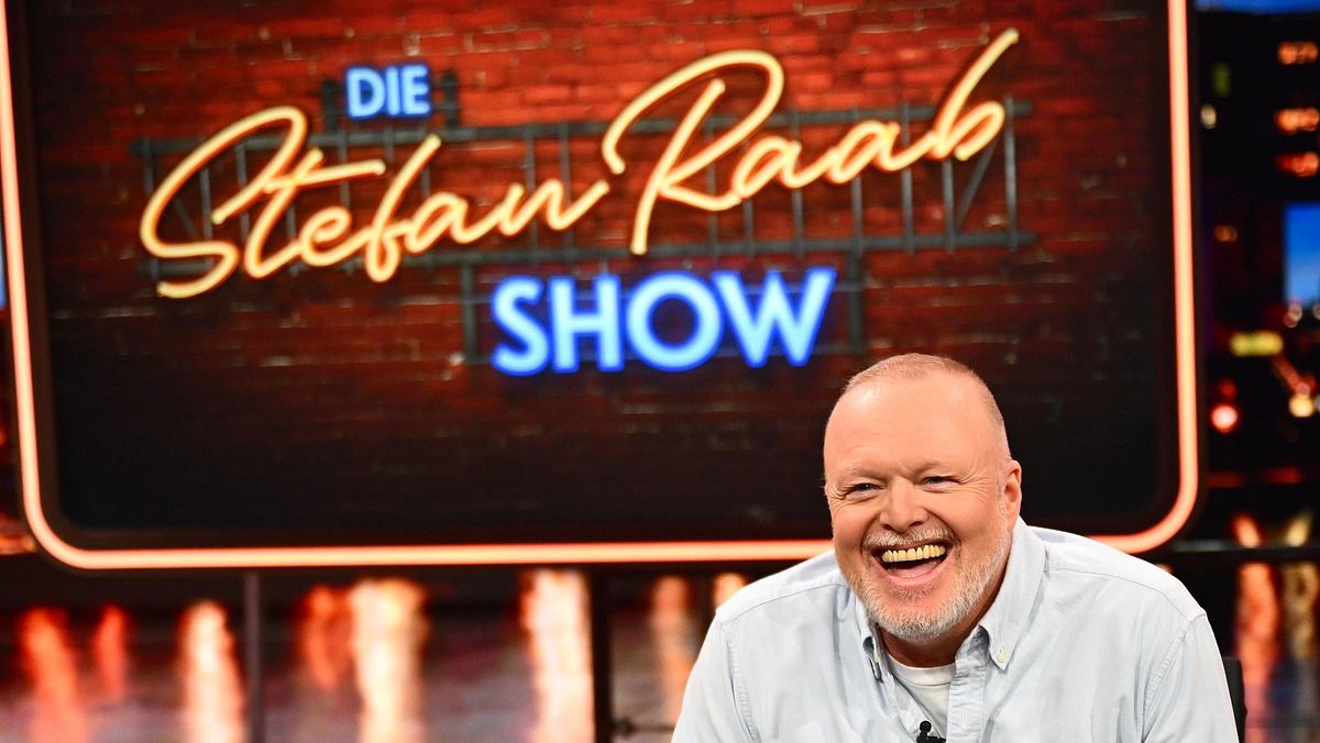 Stefan Raab sitzt lachend in seinem TV-Studio.