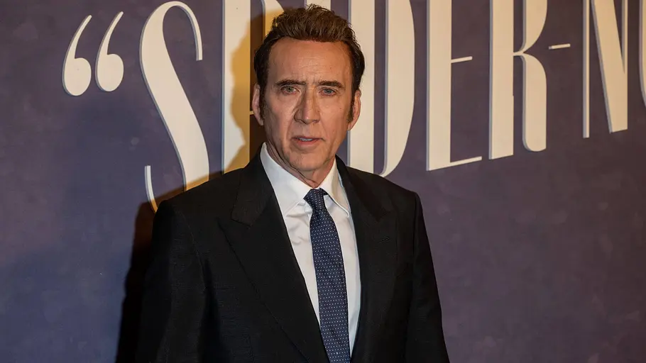 Nach „Spider-Noir“ hat Nic Cage wohl Gefallen an Fernsehserien gefunden. Nicolas Cage steht in dunklem Anzug, weißem Hemd und blauer Krawatte vor einer Wand mit großen hellen Buchstaben.