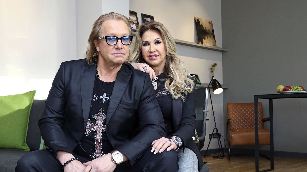 Robert und Carmen Geiss Robert und Carmen Geiss sitzen nebeneinander auf einer grauen Couch. Carmen hat ihre Hand auf Roberts Schulter.
