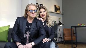 Robert und Carmen Geiss sitzen nebeneinander auf einer grauen Couch. Carmen hat ihre Hand auf Roberts Schulter. - Foto: IMAGO / Future Image