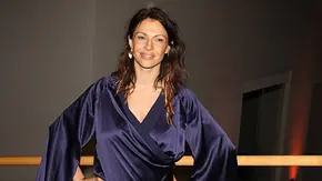 Jana Urkraft steht lächelnd in einem dunkelblauen Kleid mit weiten Ärmeln vor einem Geländer, die Hände in die Hüften gestützt. - Foto: IMAGO / POP-EYE