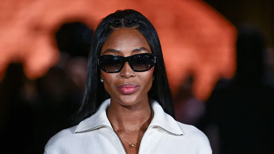 Naomi Campbell trägt eine schwarze Sonnenbrille, ein weißes Oberteil mit Reißverschluss und eine goldene Halskette.