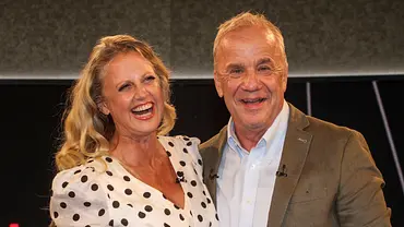 Barbara Schöneberger im gepunkteten Kleid und Hubertus Meyer-Burckhardt im braunen Sakko stehen lächelnd nebeneinander. - Foto: IMAGO / BREUEL-BILD