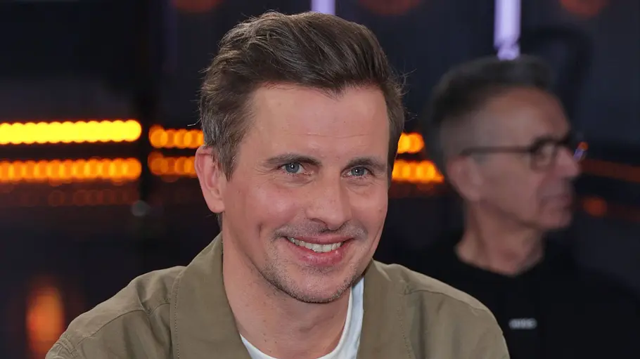 Julian Sengelmann sitzt im NDR-Studio auf einem Sessel, trägt eine lässige Jacke und lächelt entspannt in die Kamera.