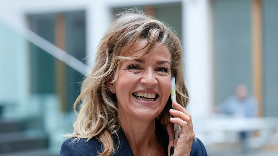 Anne-Sophie Mutter lacht und hält ein Handy ans Ohr. Sie trägt einen dunkelblauen Blazer vor unscharfem Hintergrund.