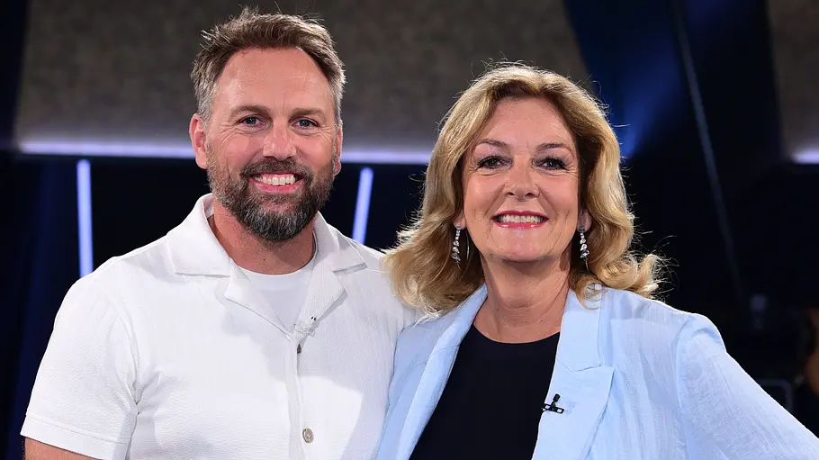 NDR Talkshow Steven Gätjen und Bettina Tietjen lächeln gemeinsam in die Kamera und posieren nebeneinander in einem TV-Studio.