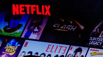 Auf dem Bild sind der rote Netflix-Schriftzug auf einem Smartphone sowie verschiedene Serien- und Filmsymbole auf einem Fernseher im Hintergrund zu sehen. Darunter sind Titel wie „Elite“, „Jupiters Legacy“ und „Money Heist“. Rechts im Bild ist der Schriftzug „Unlimited movies, shows, and more“ zu lesen. - Foto: IMAGO / Pond5 Images