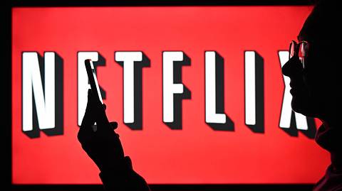 Ein Mann mit Brille steht vor einem Bildschirm, auf dem das Netflix-Logo zu sehen ist und starrt auf sein Handy - Foto:  IMAGO / NurPhoto