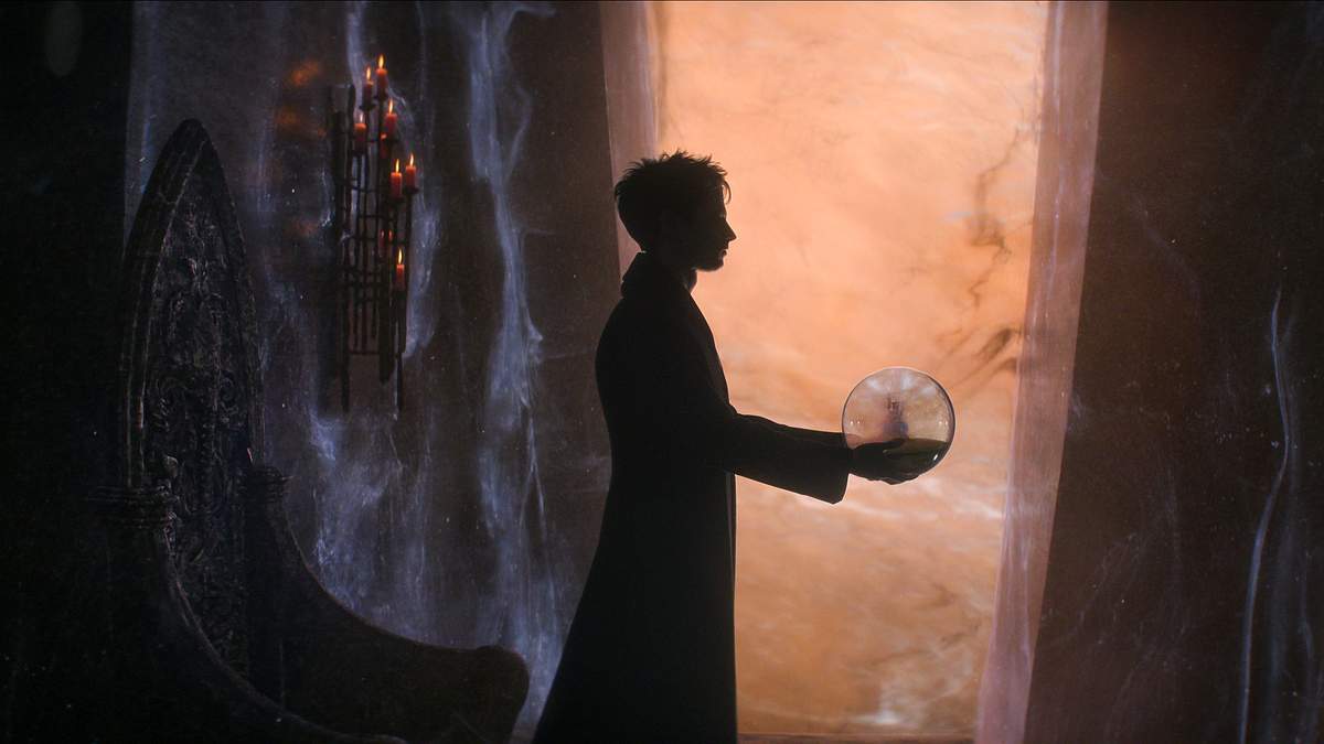 „Sandman“: Dream in einem langem Mantel. Er hält eine Kugel und blickt zur Seite.  
