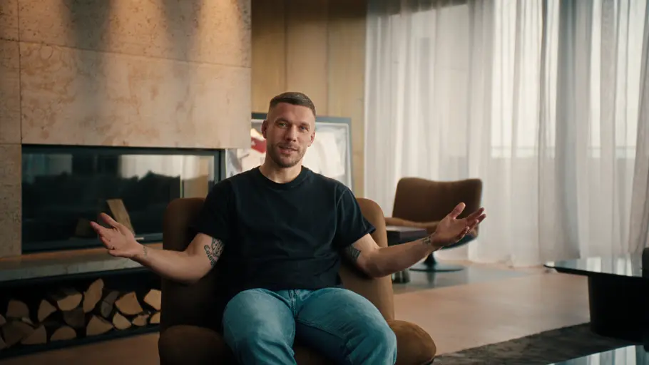 „POLDI“ Lukas Podolski sitzt in seinem Wohnzimmer auf einem Sessel und gestikuliert.