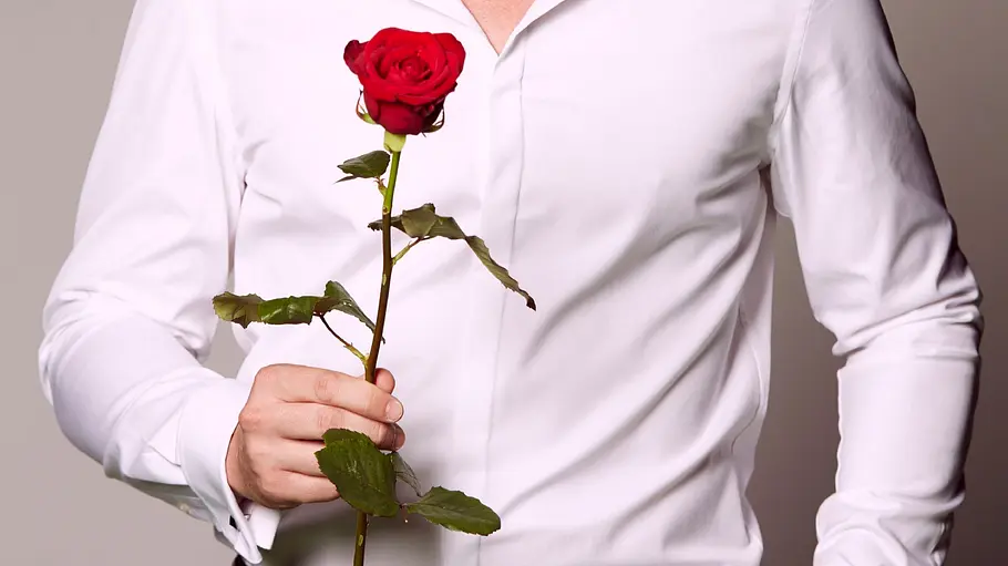 Ein Mann im weißen Hemd hält eine rote Rose in der Hand. 