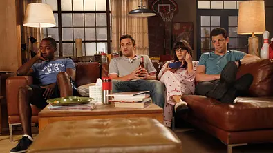 Szene aus „New Girl“: Vier Hauptfiguren sitzen gemeinsam auf einer Couch im Loft-Wohnzimmer und schauen konzentriert fern. - Foto: IMAGO / Everett Collection Szene aus „New Girl“: Vier Hauptfiguren sitzen gemeinsam auf einer Couch im Loft-Wohnzimmer und schauen konzentriert fern. - Foto: IMAGO / Everett Collection