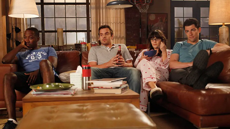 New Girl Szene aus „New Girl“: Vier Hauptfiguren sitzen gemeinsam auf einer Couch im Loft-Wohnzimmer und schauen konzentriert fern.