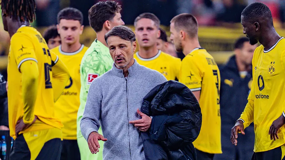 Coach Nico Kovac mit Jacke über dem Arm, umgeben von Fußballspielern in typischen gelben BVB-Heimtrikots.