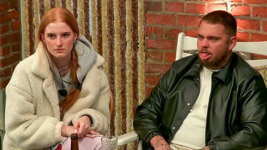 Nico Legat Laura Sommerhaus-Ausstieg Laura im hellen Mantel und Nico Legat in schwarzer Lederjacke sitzen am „Sommerhaus“-Tisch mit Flaschen und Gläsern vor einer Backsteinwand.