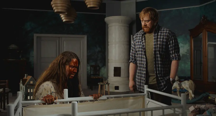 Nightborn Szenenbild Seidi Haarla und Rupert Grint stehen im Szenenbild an einer Krippe. Sie ist mit Blut beschmiert, er schaut sie besorgt an.