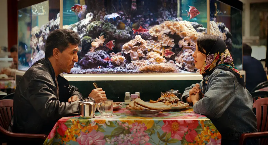 Ein Mann und eine Frau sitzen sich im Restaurant gegenüber. Hinter ihnen ist ein Aquarium zu sehen.
