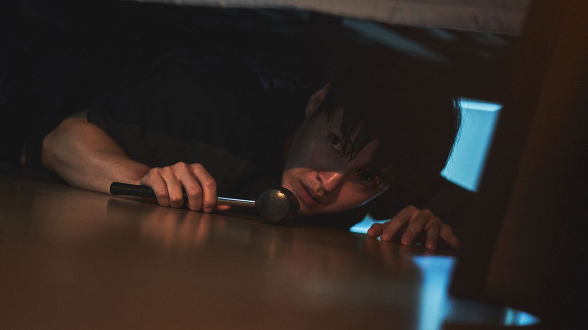 No Woo-sung versteckt sich mit einem Hammer unter dem Bett.